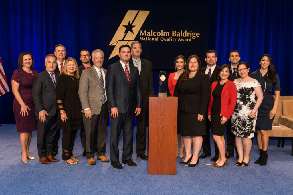 CSSD staff members pose for a photo opp on stage with the Baldrige Award Crystal and banner
